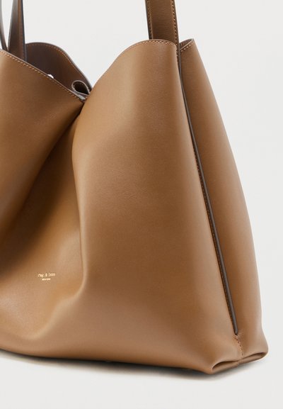 Μαλακή τσάντα ώμου από καφέ δέρμα με φαρδιές λαβές και ελάχιστες ραφές, που παρουσιάζει μια λεία, στιβαρή επιφάνεια και διακριτικό λογότυπο μάρκας.