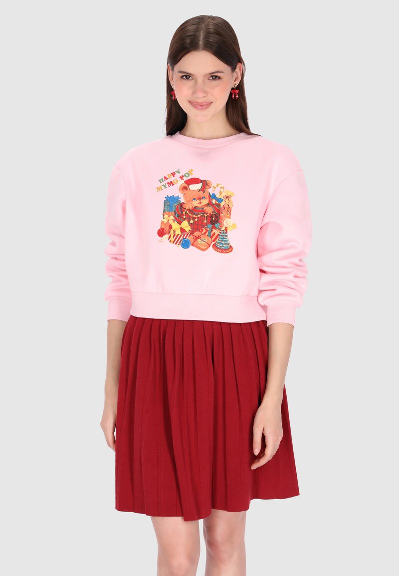 Sudadera rosa con un gráfico que muestra un oso y regalos, combinada con una falda plisada roja. Tela suave, ajuste casual y colores vibrantes.
