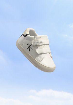 Baskets blanches pour tout-petit Calvin Klein avec deux bandes Velcro sur fond d'un ciel bleu clair.