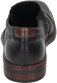 Black leather shoe with a smooth texture, curved back, rounded toe, and a brown leather accent on the heel. Stitched welt detail visible.