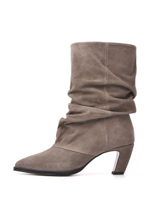 Botte mi-mollet en daim taupe décontractée, avec un bout pointu, un petit talon bloc incliné et une semelle noire sur fond blanc.