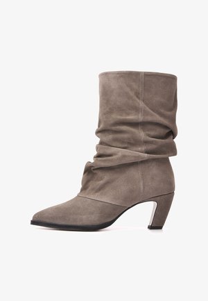 Botte mi-mollet en daim taupe décontractée, avec un bout pointu, un petit talon bloc incliné et une semelle noire sur fond blanc.