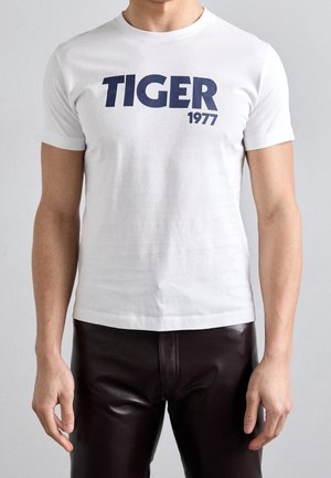 T-shirt en coton blanc avec un impression audacieuse "TIGER 1977" en marine sur le devant, avec des manches courtes et un col rond classique.
