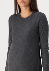 Grå ribbad långärmad topp med rund halsringning, med en mjuk textur och sidospalter för ökad rörelsefrihet.