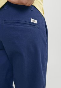 Mørkeblå bukser i bomull, med en baklomme med etikett. Glatt tekstur, klassisk design og skreddersydd passform.