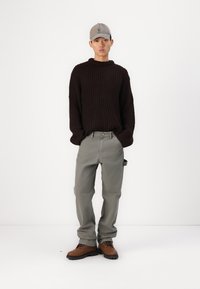 Mörkbrun ribbad tröja, grå byxor, bruna snörskor och en ljusgrå keps. Outfiten har en avslappnad passform och enkel design.