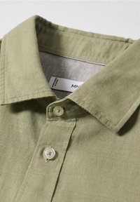 Camisa abotonada verde claro hecha de tejido texturizado con un cuello clásico y botones transparentes, con una etiqueta cosida en el interior del cuello.