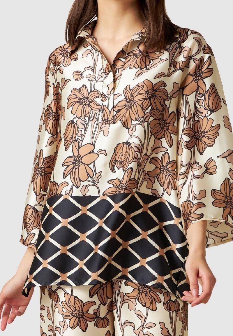 Blusa di satin con un motivo floreale marrone su sfondo avorio, con orlo geometrico nero e colletto con bottoni.