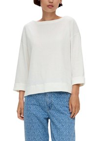 Valkoinen neulepaita, jossa on teksturoitu kangas, leveä kaula-aukko ja kolmen neljänneksen hihat. Yhdistetty vaaleansinisiin kuvioituihin farkkuihin.