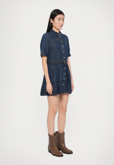 Rifľové šaty-košeľa s krátkymi nafúknutými rukávmi, zapínanie na gombíky vpredu, viacvrstvová sukňa a priliehavý pás. Nosené s hnedými členkovými čižmami.