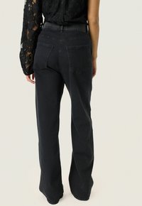 Schwarze Jeans aus Denim mit hoher Taille, geradem Bein und zwei Gesäßtaschen. Glatte Textur mit einem dezenten, ausgewaschenen Finish.
