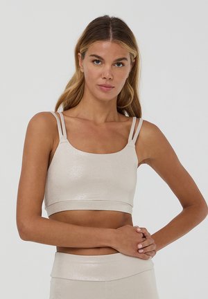Jasnobeżowy crop top wykonany z błyszczącego, elastycznego materiału. Posiada podwójne, wąskie ramiączka oraz dopasowany krój z szerokim dołem.