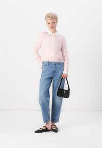 Suéter de punto rosa claro con dobladillo acanalado, cuello blanco, jeans de tiro alto azul, zapatos planos negros y un pequeño bolso negro.