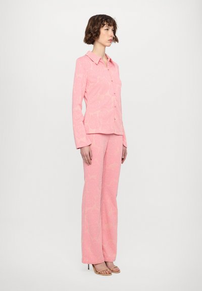 Pink floral-patterned blouse with a collar, button closure, and long sleeves paired with matching flared pants and strappy sandals.
