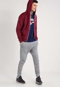 Burgunderfarget zip-up hettegenser med hette og frontlommer, kombinert med lys grå smale joggebukser med teksturert mønster og elastiske mansjetter.