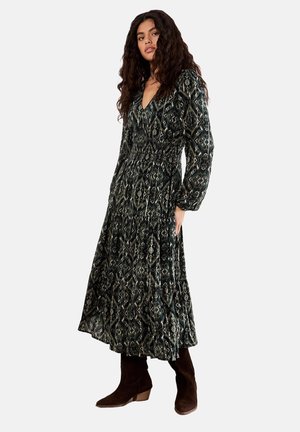 Abito lungo scuro con motivo, scollatura a V, vita arricciata e maniche ampie. Abbinato a stivali alla caviglia in suede marrone. Design floreale geometrico.