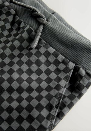 Pantaloni jogger în carouri alb-negru, cu talie elastică și șnur. Prezintă un material neted cu o textura mată.