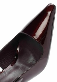 Zapato de charol burdeos con punta afilada, diseño de lado abierto y textura suave. Presenta un sutil bordado en los bordes.