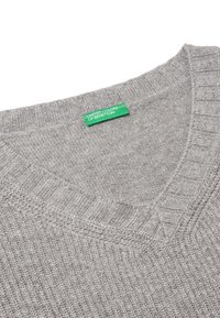 Grauer gestrickter Pullover mit einem V-Ausschnitt-Design. Verfügt über gerippte Akzente an den Ärmeln und am Kragen. Das Etikett zeigt "United Colors of Benetton" in Grün.