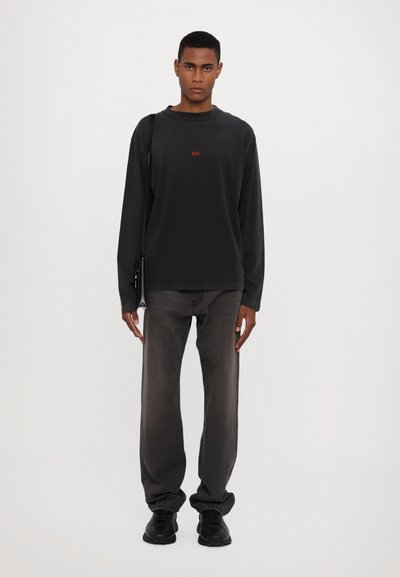 Crna majica dugih rukava s crvenim "424" logotipom, u paru s sivim trapericama i crnim tenisicama. Jednostavna tekstura, opušteni kroj i minimalistički dizajn.