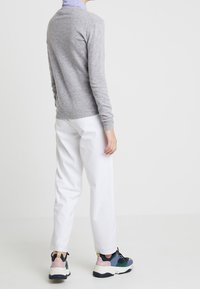 Grå tröja, vita byxor och flerfärgade sneakers. Tröjan har en rund hals, åtsittande ärmar och är gjord av ett mjukt stickat material.