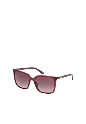 Lunettes de soleil carrées rouges avec des verres dégradés, branches fines, et logo doré près de la charnière. Fabriquées en plastique léger.