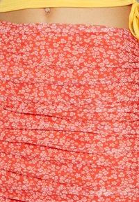 Saia floral vermelha com textura franzida, apresentando pequenas flores brancas. Feita de tecido leve, projetada com detalhes de pregas discretas.