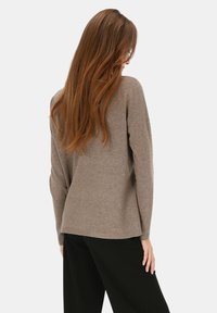 Brązowy sweter z długim rękawem, miękka faktura, luźny krój, lekko wydłużony tył, noszony na czarnych spodniach.