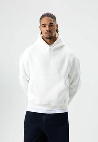 Witte hoodie met kangoeroezak, geribbelde manchetten en zoom, met een comfortabele pasvorm en zachte textuur. Draagt over een wit overhemd.