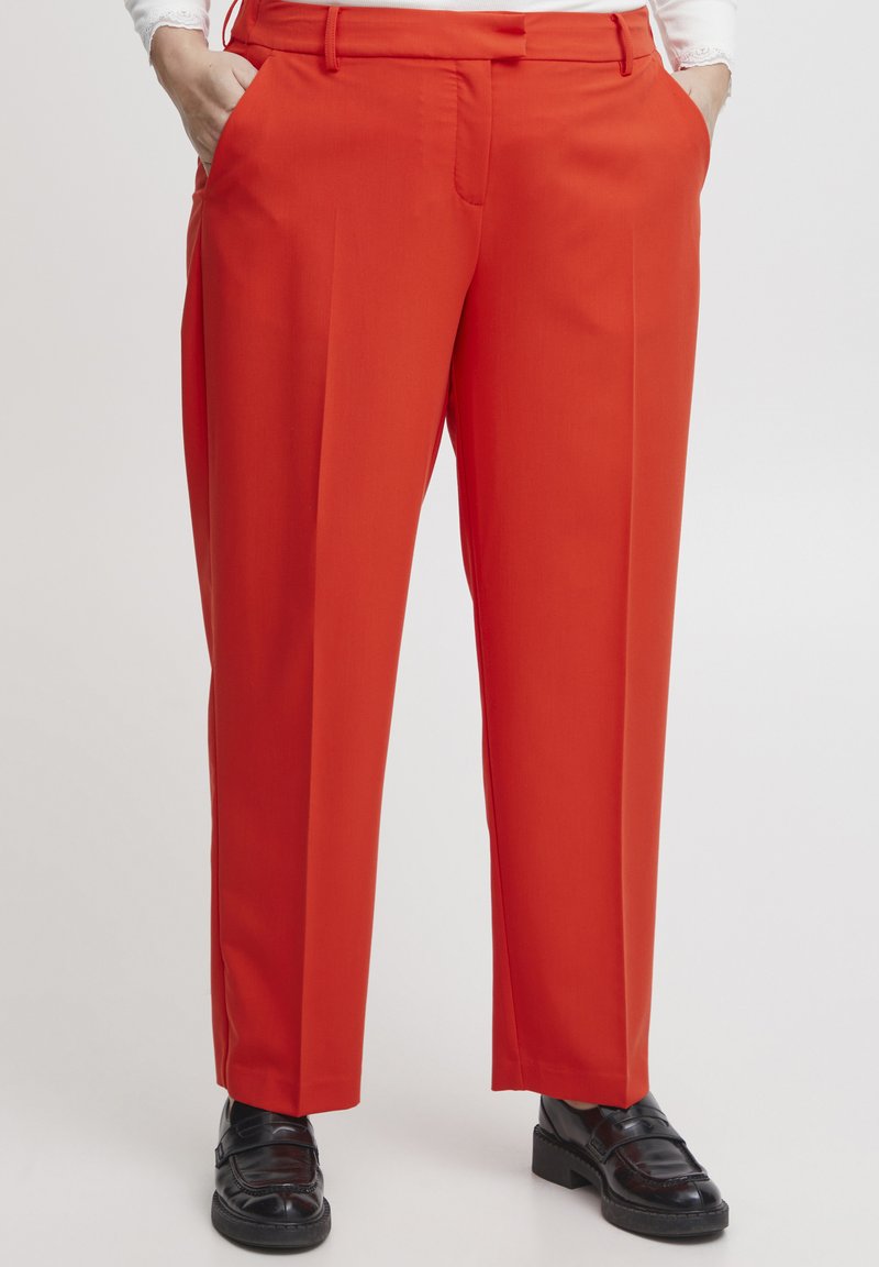 Pantalons ajustés rouges avec une coupe droite, dotés de poches latérales et d'une texture lisse. Portés avec des mocassins noirs.