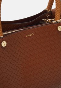 Bruine gevlochten leren handtas met ritssluiting, voorzien van een merklogo, goudkleurige metalen accenten en gevlochten handvatten.