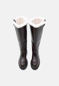 Botine lungi din piele maro, cu căptușeală moale albă, talpă plată neagră și mânere laterale pentru a fi ușor de purtat. Textură netedă și design structurat.