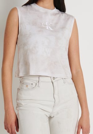 Ærmeløs, lysegrå tie-dye croptop med hvidt CK-logo, kombineret med højtaljede lyse beige jeans med lille logo på lommen.
