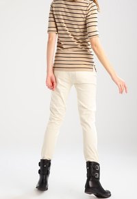 Striped beige short-sleeve top, cream fitted pants, and black ankle boots with buckle accents, viewed from behind. Plain background.