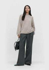 Jasno-beżowy, oversize sweter z prążkowanym wykończeniem, w zestawie z szerokimi szarymi spodniami. Czarna torba z detalem na sznurku i czarne buty w szpic.
