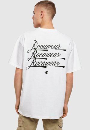 Hvid bomulds t-shirt med stort sort kursiv "Rocawear" tekst trykt på ryggen. Kortærmet og afslappet pasform.