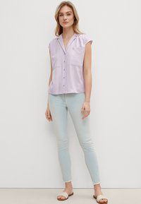 Light lavender short-sleeve blouse with a collared neckline, two front pockets, and subtle button detail, paired with light blue skinny jeans.