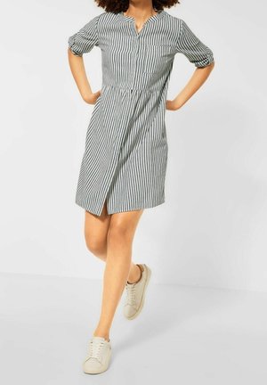 Robe boutonnée à rayures noir et blanc, manches courtes, légère forme trapèze et poche avant. Associée à des baskets beige.