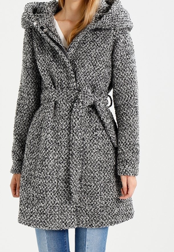 Femme portant un manteau gris texturé ceinturé avec capuche, debout les mains relâchées le long du corps, associée à un jean bleu.