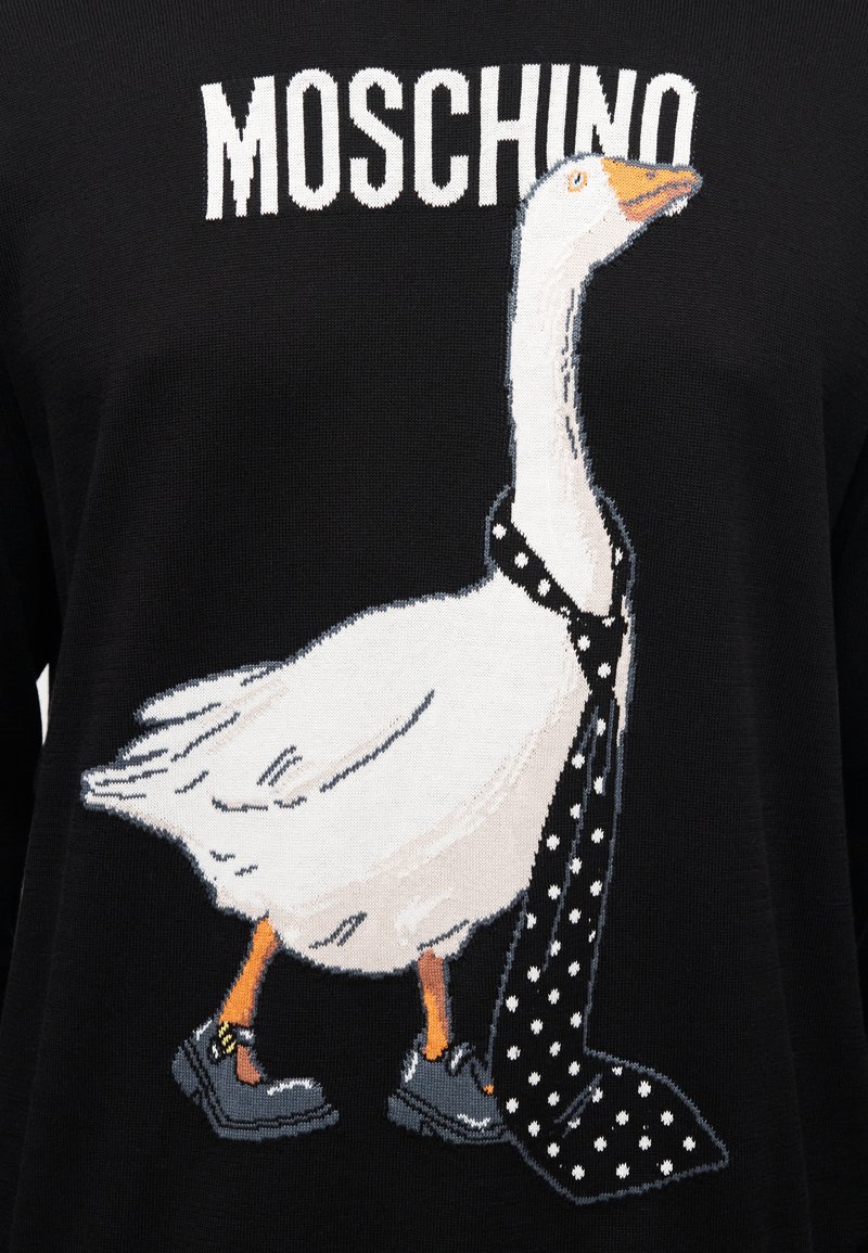 Schwarzer Pullover mit einer Comic-Gans, die eine gepunktete Krawatte und schwarze Schuhe mit goldenem Akzent trägt. "Moschino"-Logo darüber.