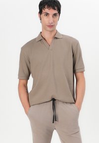 Short-sleeve, tan polo shirt with a v-neck and textured fabric, paired with light beige pants featuring a drawstring waist.