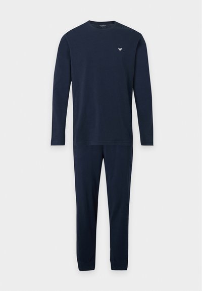 Ensemble haut à manches longues bleu marine et pantalon assorti avec un petit logo blanc sur la poitrine gauche, présenté sur un fond uni.