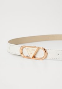 Cintura in ecopelle bianca con fibbia triangolare color oro e logo "GUESS U.S.A." con particolare a forma di punto interrogativo.