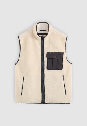 Vest din fleece crem cu închidere cu fermoar negru, buzunare laterale și un buzunar frontal cu detaliu cu nasture. Se observă margini contrastante.