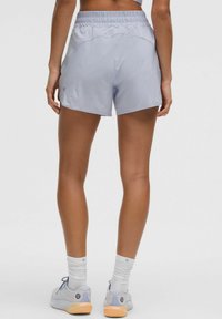 Ljusblå träningsshorts med elastisk midja och sidofickor, tillverkade av ett slätt tyg. Bärs med grå och blå sneakers.