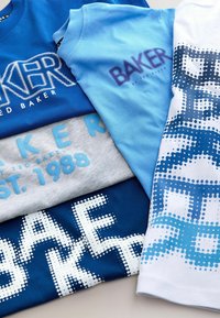 Cinq t-shirts empilés, aux couleurs bleu et gris. Les motifs incluent du texte en différentes polices et des motifs de points. Matière en coton, manches courtes.