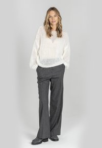 Biały sweter z otwartym splotem, z długimi rękawami, w połączeniu z szarymi spodniami o szerokiej nogawce i czarnymi butami. Miła w dotyku, swobodna forma i luźny krój.