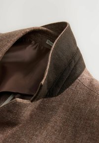 Collar de lana marrón con un acento marrón más oscuro; forro interior suave con un ligero brillo; contrastes de textura notables entre los materiales.