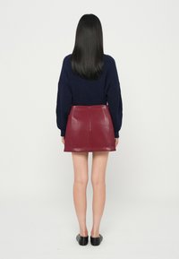 Maglione a coste blu navy abbinato a una mini gonna in pelle color bordeaux, con cerniera sul retro e una texture liscia e lucida. Scarpe nere flat completano il look.