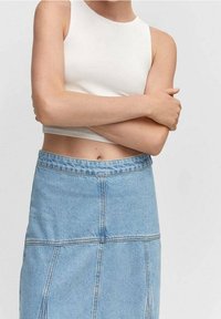 Valkoinen hihaton crop-top, joka on yhdistetty vaaleansiniseen farkku-mekkoon, jossa on näkyvät ompeleet ja korkea vyötärödesign.